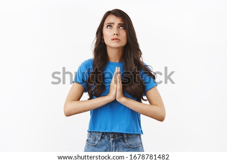 Dear lord make my dream come true, please hear prayers. Worried supplicating brunette woman clasp hands together in pray, looking at sky frowning worried, standing white background