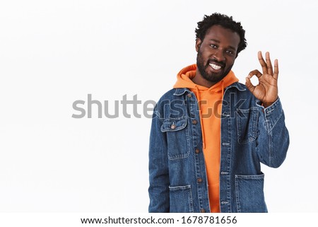 Cool stylish, handsome african-american bearded man in orange hoodie, denim jacket, showing his permission or judgement, make okay ok approval sign and smiling, like your choice, white background