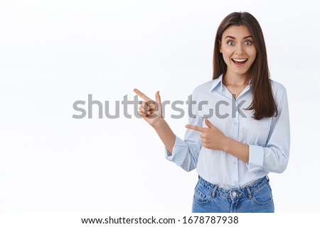 Surprised young successful working woman in blue blouse look impressed as seeing something unexpecting and awesome, pointing finger left sharing great news with you, white background