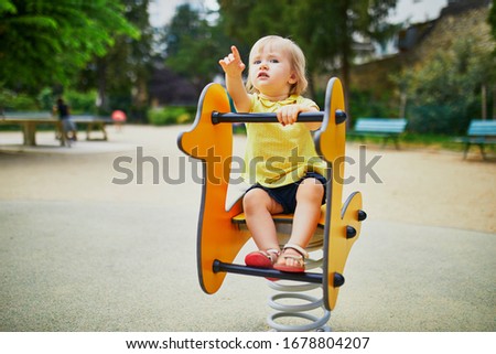 Adorable toddler girl having fun on spring rider on playground. Outdoor activities for kids