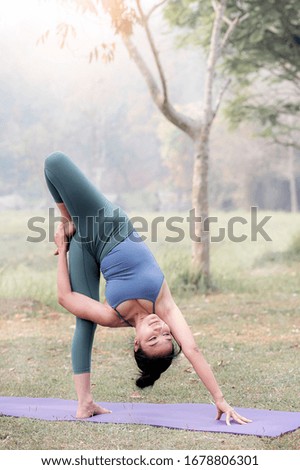 Young beautiful asian woman in sportswear practicing yoga in the park, vertical view.