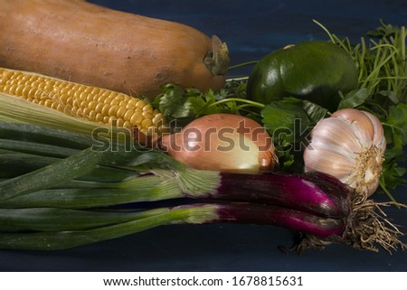 some raw vegetables on a blue table. Pumpkin, onions, green pepper, garlic. corn