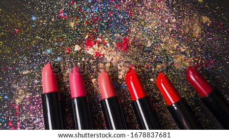 Cosmetics and beauty industry, a set of lipsticks on a background of loose powder and eye shadow, dark textured background