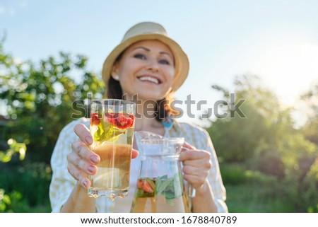 Close-up of jug and glass with natural herbal mint strawberry drink in hands of woman. Summer cold refreshment drinks, healthy vitamin homemade drinks, copy space