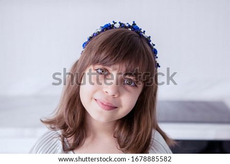 Portrait of adorable brunette Caucasian girl smiling at camera, while wearing blue pearl headband in her home