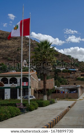peruvian flag hoisted on mast in street surrounded by houses in andean town in peru