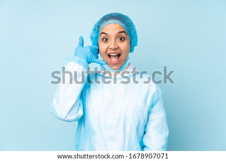 Young surgeon Indian woman in blue uniform making phone gesture. Call me back sign