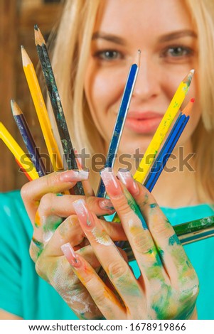 Humorous photo of great artist. Portrait of beautiful young woman with colored pencils. Selective focus on pencils.