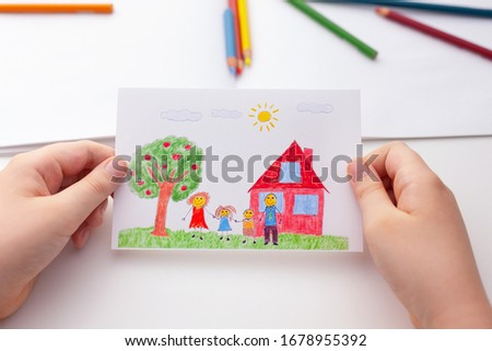 Child holding a drawing with a happy family and an apple tree and a house. Close up. 