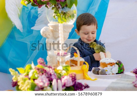 Cute boy with easter duckling in hands at the table with easter treats with eggs and easter cake. Easter concept