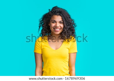 Portrait of beautiful smiling dark skinned girl wearing bright colored yellow t-shirt isolated over blue background.