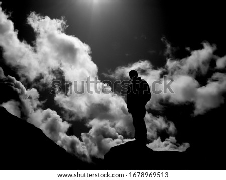 A single person silhouetted against a dramatic cloudscape