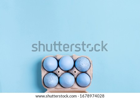 Papercraft container with handmade painted pastel blue Easter eggs on a same color background. Flat lay.