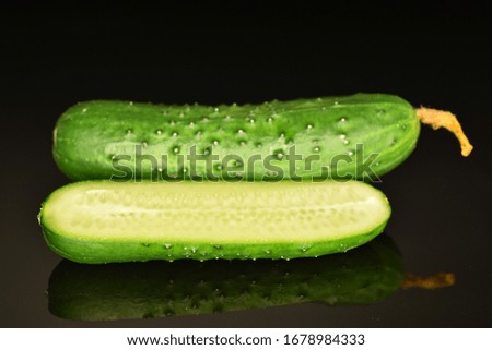 One whole and one half green organic ripe juicy cucumber, close-up, on a black background.