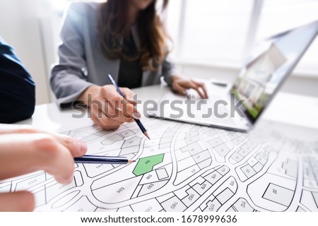 Two People Looking At Cadastre Map With Laptop On Desk Royalty-Free Stock Photo #1678999636