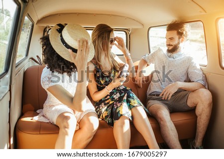 Three best friends travel in a minivan bus and explore new places. Two girls and one boy having good times. Taking pictures and selifies. Hugging and kissing eachother