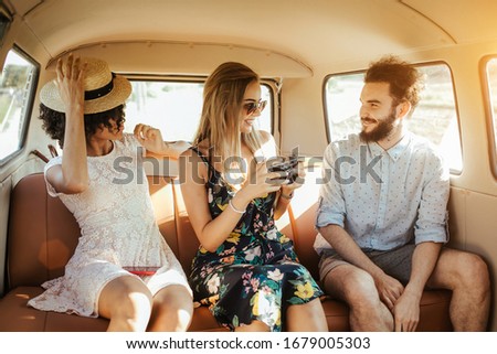 Three best friends travel in a minivan bus and explore new places. Two girls and one boy having good times. Taking pictures and selifies. Hugging and kissing eachother