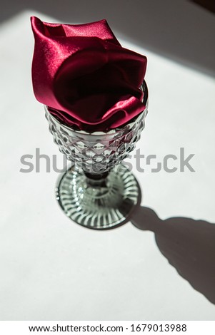 Photo of a glass on a white background in sunlight with a burgundy cloth. Wine imitation