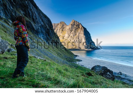 Woman hiker in colorful jacket enjoys the view at famous Kvalvika beach hidden between steep cliffs of Lofoten mountains, Norway