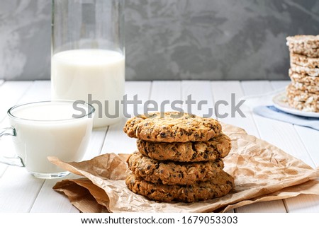homemade oatmeal cookies with chocolate and milk. baking, milk in a decanter and a stack of cookies on a wooden table. healthy food