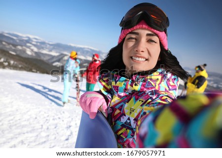 Young woman with snowboard taking selfie at ski resort. Winter vacation