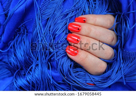 Female hands with red manicure on blue background. Stylish fashionable woman's manicure. Nail polish. Artistic manicure. Modern style.