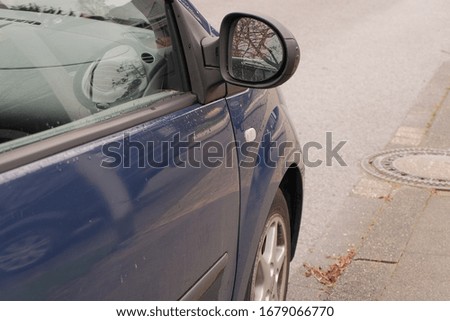 A closeup of a blue car with raindrops on it on the street with a blurry background