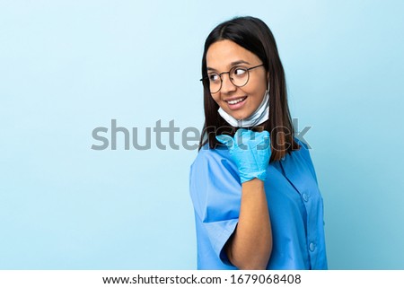 Surgeon woman over isolated blue background pointing to the side to present a product