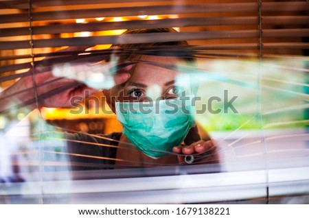 Worried Woman looking through window from home in quarantine during Coronavirus. Anxiety Woman in self distancing isolation due to Covid-19.Stay at home in time of pandemic concept  Royalty-Free Stock Photo #1679138221