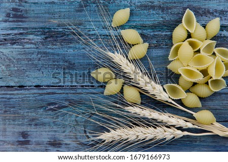 Flat lay. Food background. Dry pasta scattered on a blue wooden table. Textured pasta background. Wheat spikelets and pasta of different shapes on a blue surface. Close-up, free space, horizontal.