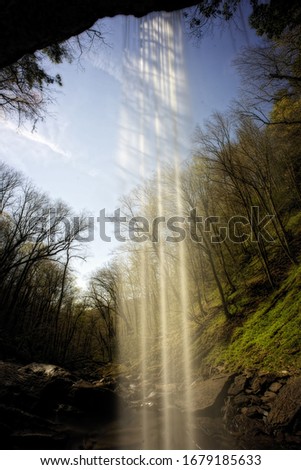 A vertical picture of a waterfall surrounded by rocks and greenery under the sunlight