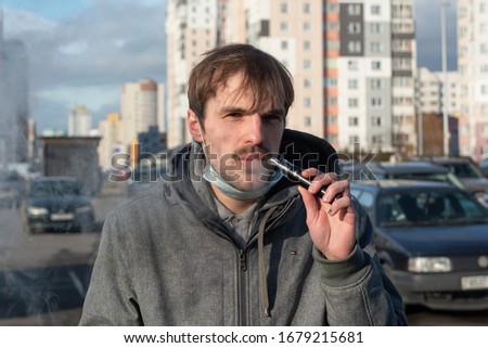 the guy on the street smokes an electronic cigarette. Blows thick steam through the nose. on the face on the chin a medical white mask. Protection against viruses, coronavirus, airborne diseases
 Royalty-Free Stock Photo #1679215681