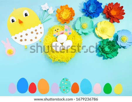 Child made crafts his own hands at Easter. Handmade nest with eggs, flowers, chicken, chicken in an egg, bunny. Cute art creativity on blue background. Flat lay, top view, close up, copy space