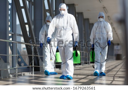 People in virus protective suits and mask disinfecting buildings of coronavirus with the sprayer, Royalty-Free Stock Photo #1679263561