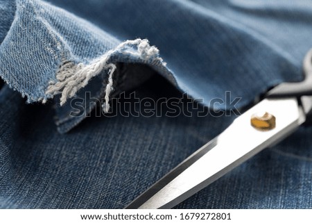 Torn blue denim cotton fabric trousers with scissors - jeans fashion mending or repair concept, selective focus