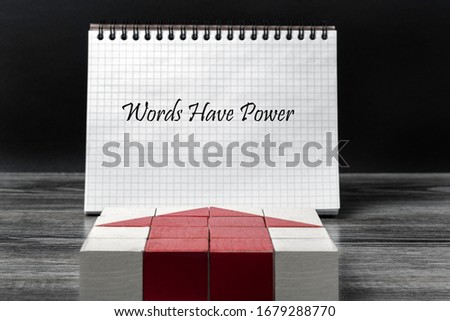 A mosaic of children’s cubes in the shape of an arrow indicates an open notebook. The inscription in the notebook: "Words have power."