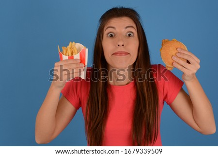 young woman in a pink t-shirt holds a potato burger on a blue background