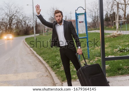 Hey, wait, I need a ride. A man with a beard, in a suit, stands at the station with his suitcase. He raised his hand and hoped to find transportation