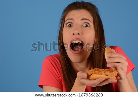 surprised woman in pink t-shirt holds hamburger on blue background