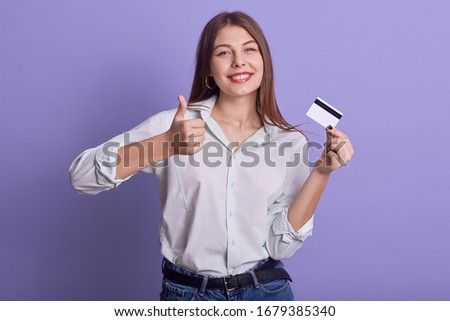 Image of cheerful positive charismatic youngster doing credit payments, making gesture, showing sign of approval super, holding credit card, wearing casual clothes, having tender smile. Money concept.