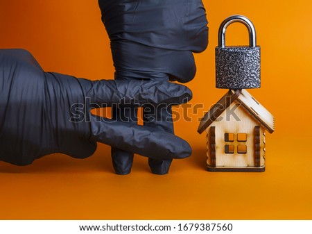 of the fingers in a latex glove of the black color sign,a wooden house and a padlock,concept of house arrest,isolation,arrest for going outside,pandemic ,violation of the law Royalty-Free Stock Photo #1679387560
