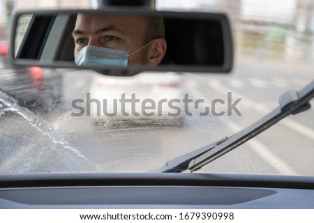 Reflection of face of middle aged man in the medical mask for protect himself from bacteria and virus while driving a car. rear view mirror.car wipers clean windshield. Coronavirus. Pandemic  Royalty-Free Stock Photo #1679390998