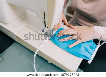 Woman hands using the sewing machine to sew the face medical mask during the coronavirus pandemia. Home made diy protective mask against virus. Royalty-Free Stock Photo #1679393293