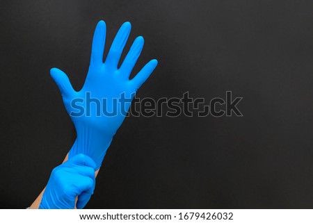 Female hands in blue medical protective gloves. Doctor, surgeon or nurse. Means of protection against germs and dirt. Black background, copy space.