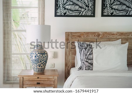 Element of decor at white interior  in comfortable bedroom with lamp at wooden, old nightstand near bed inside of lovely house