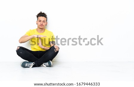 Caucasian man sitting on the floor making time out gesture