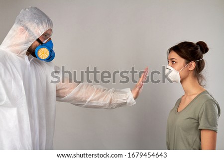 Stay away from me! Don't come closer. Man in protective clothing covid19 showing stop gesture to a girl isolated on grey background. Royalty-Free Stock Photo #1679454643
