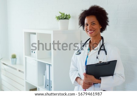 Portrait of beautiful smiling female african american doctor standing in medical office. Health care concept, medical insurance, copy space. Royalty-Free Stock Photo #1679461987