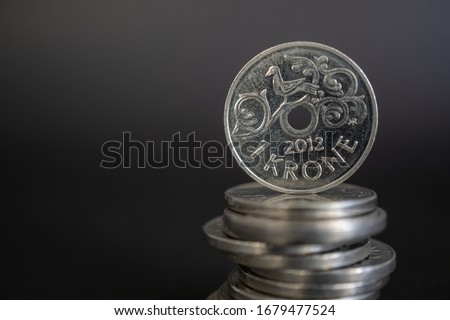 One Norwegian krone coin (NOK) standing on stack of coins against black background. Budget and Economy of Norway.