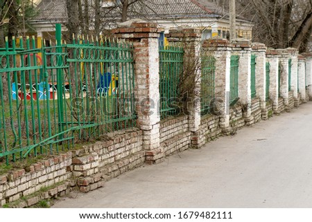 old brick fence with green metal bars on the background of the playground